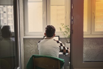 Back view of a man sitting at a desk using a laptop at sunset