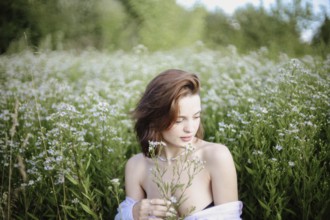 A woman sits thoughtfully with flowers, surrounded by lush greenery