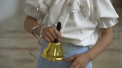 Little girl ringing a bell in the school classroom, closeup