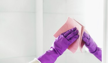 Cropped view of housekeeper woman hand in purple rubber gloves polishing mirror with pink cloth rag