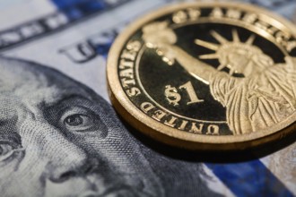 One dollar coin, The Statue of Liberty, on hundred dollars bills. Closeup, macro shot