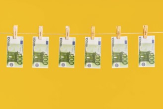 Money laundering, euro banknotes hanging on rope over yellow studio background. Finance,