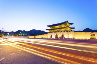 Colorful streaking headlights of cars passing in front of lighted gate of Gwanghuamun, entrance to