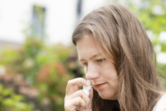 Young woman suffers from hay fever and sprays her nose outdoors, Freiburg, Baden-Württemberg,