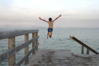 Boy jumps into water, wooden jetty