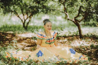 Happy girl in national folk costume sitting on the grass