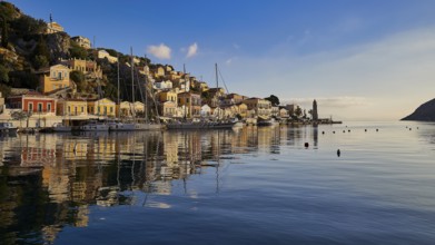 Picturesque harbour with reflecting buildings in the water. Atmospheric sky at sunset, Symi town,