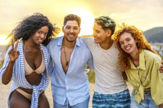 Four multi ethnic friends hug each other, enjoying a summer sunset at the beach, with one of them