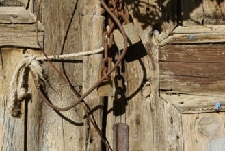 Old wooden door with rusty chains and locks, weathered in the sunlight, Symi Town, Symi,