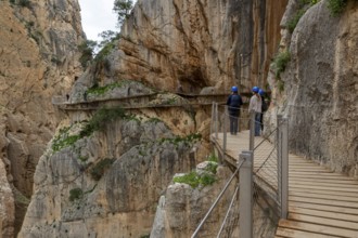 People with helmets walking on the wooden path Caminito del Rey along a rocky cliff, Malaga, Spain,