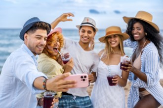 Multi ethnic friends taking selfie on beach while drinking juice, enjoying summer vacation together