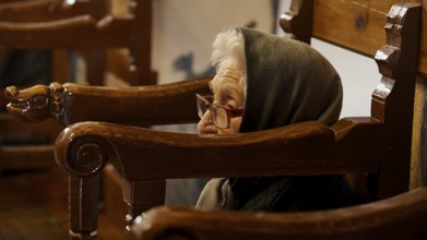 An elderly woman with a hood, sitting in a chair, deep in thought, Easter 2025, Church of the