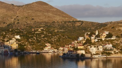View of a settlement on a hill with warm light, calm water in the foreground, Symi Town, Symi,