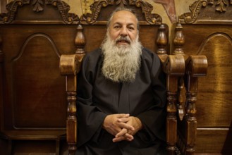 Papas Nektarios, Elderly man with beard on a wooden chair in a quiet, monastic environment,