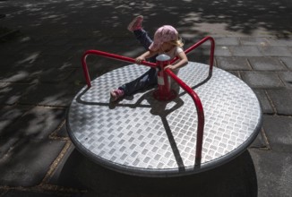 Outdoor shot, little girl, 3 years old, blonde, playing on a merry-go-round, children's playground,