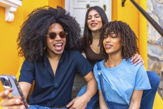 Three happy young friends are taking a selfie with a smartphone while sitting on the stairs of a