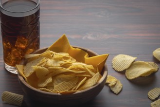 Wooden bowl with crisps and glass of cola on a table