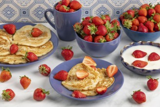 Pancakes and fresh strawberries on plates with yoghurt, blue crockery