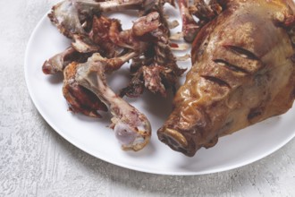 Roast pork head, with remnants of bones and meat, on a white platter, no people, close-up