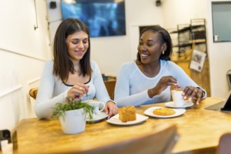 Two young women enjoying a coffee break, chatting and laughing together in a vibrant, modern cafe