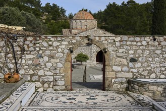 Path of mosaic stones leads to a church, surrounded by a high stone wall and trees, Thari