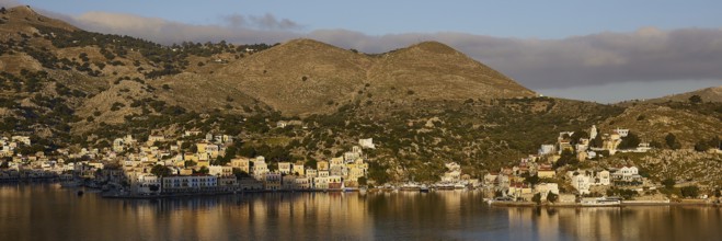 Island with houses and mountains in the background, calm water, atmospheric landscape, Symi town,