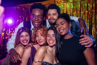 Group of cheerful elegant friends posing together for a photo at nightclub party with disco lights