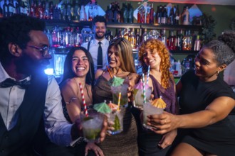 Cheerful multi ethnic friends raising cocktail glasses for a celebratory toast in a nightclub,