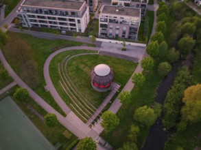Aerial view of a modern wooden construction in the park with trees and surrounding buildings at
