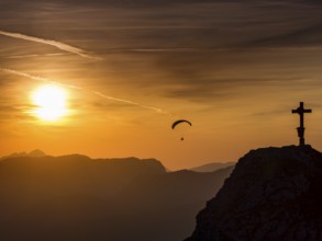 Paraglider flying next to the summit cross of the small Jenner at sunset, Reiteralpe in the