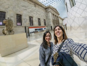 Two happy female tourists are taking a selfie with a fisheye lens at the british museum's great