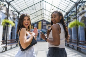 Two cheerful female friends walking away while waving and holding a reusable coffee cup in the city