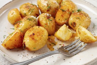 Half-eaten fried new potatoes, with butter and dill, on a white plate, with a fork, at home, no