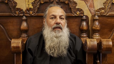 Portrait of a bearded man in black clothes, sitting on a wooden chair, Papas Nektarios, Monastery