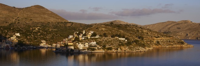 Island in a quiet bay, framed by mountains and bright sky in the morning light, Symi Town, Symi,