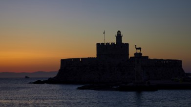 Fortress by the sea silhouetted against a colourful sunrise, dawn, Fort of Saint Nikolaos, Mandraki