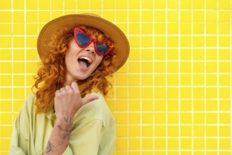 Cheerful influencer pointing her thumb while smiling, wearing a straw hat and heart shaped