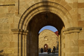 View through a stone arch onto people sitting and chatting in front of a church, Easter 2025,
