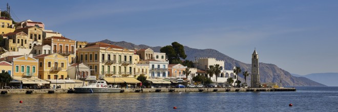 Historic coastal buildings, a striking tower and the sea under a bright blue sky, Symi Town, Symi,