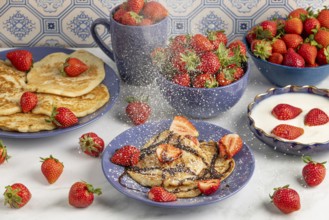 Icing sugar falls on pancakes with strawberries and chocolate syrup, fresh strawberries and yoghurt
