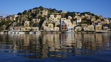 Colourful house front on the coastline with harbour and boat reflections in the water, Symi Town,