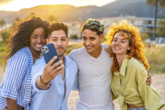 Four cheerful young friends of diverse backgrounds capturing a joyful selfie at sunset on a