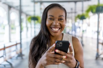 Smiling businesswoman using mobile phone in bright, modern office space, enjoying convenient