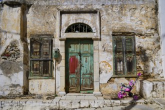 Weathered old house facade in an urban environment, pink pram in front of it, Symi Town, Symi,