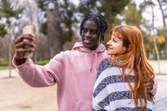 Young multiracial couple smiling together while capturing a joyful selfie with a smartphone in a