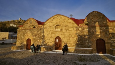 Stone church with rounded roofs and some people walking along in the evening light, Easter 2025,