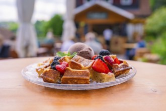 Fresh waffles with berries and ice cream on a table in front of a cosy outdoor café, Cafehäusle