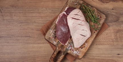 Fresh raw duck breasts, on a wooden chopping board, with herbs and spices, no people