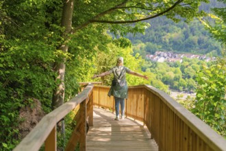 A person walks on a wooden path with outstretched arms through nature, Panorama Holzsteg, Calw,