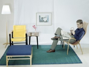 In the 1950s 1960s. A man is sitting comfortably in an armchair reading the newspaper and having a